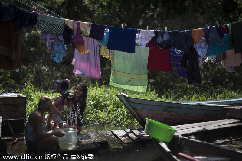 Deux jeunes filles font prendre un bain à leur petite soeur, près de leur maison flottante dans le ? Lago do Janauari ?, près de Manaus, au Brésil, le 20 mai 2014. Manaus est l’une des villes h?tes de la Coupe du Monde 2014 au Brésil. [Photo/IC]