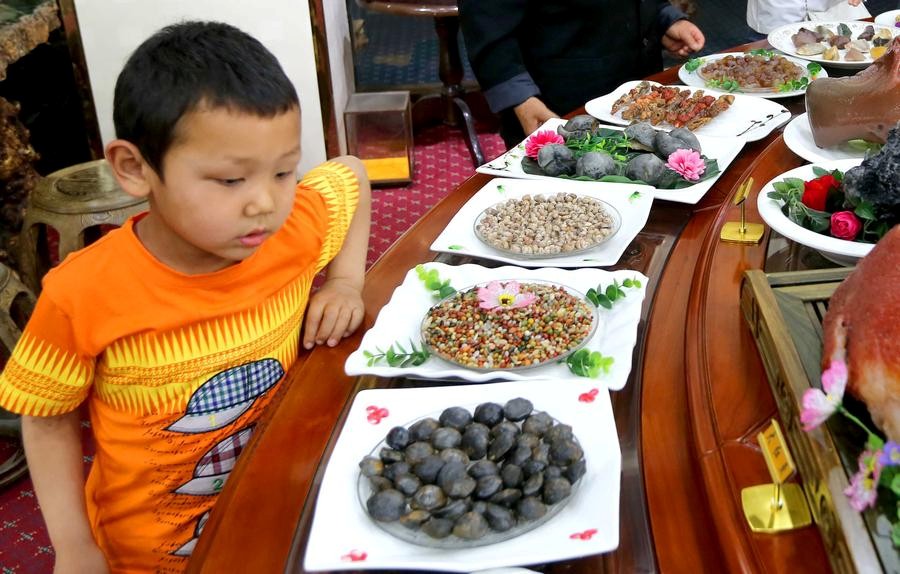 Un jeune visiteur admire des plats faits en pierre lors d’une exposition dans la préfecture de Hami, lundi dans la Région autonome ou?goure du Xinjiang. [Photo / Xinhua]