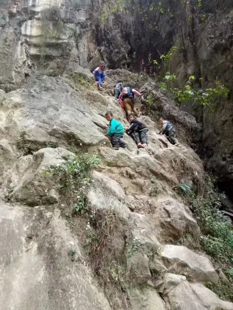 Un adulte accompagne des élèves alors qu'ils grimpent la falaise pour se rendre à l'école. (Photo d'archives)