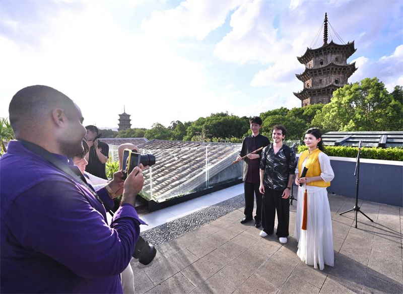 Un touriste étranger (au centre) prend une photo avec des artistes du Nanyin de Quanzhou sur le site pittoresque de la rue de l'Ouest à Quanzhou, dans la province du Fujian (sud-est de la Chine), le 20 juin 2025. (Xinhua/Jiang Kehong)