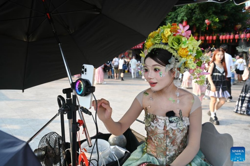 Une membre du personnel portant un couvre-chef fleuri présente des produits photographiques de voyage locaux via une diffusion en direct depuis le village de Xunpu, à Quanzhou, dans la province du Fujian (sud-est de la Chine), le 18 ao?t 2025.(Lin Shanchuan/Xinhua)